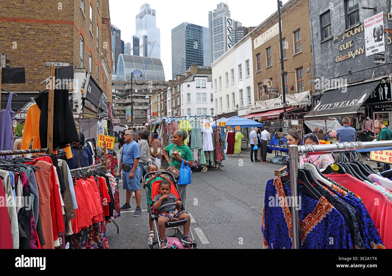 Petticoat Lane Market street scene on Wentworth Street, Spitalfields, London E1 7TB, with clothing stalls in the foreground and City of London offices Stock Photo