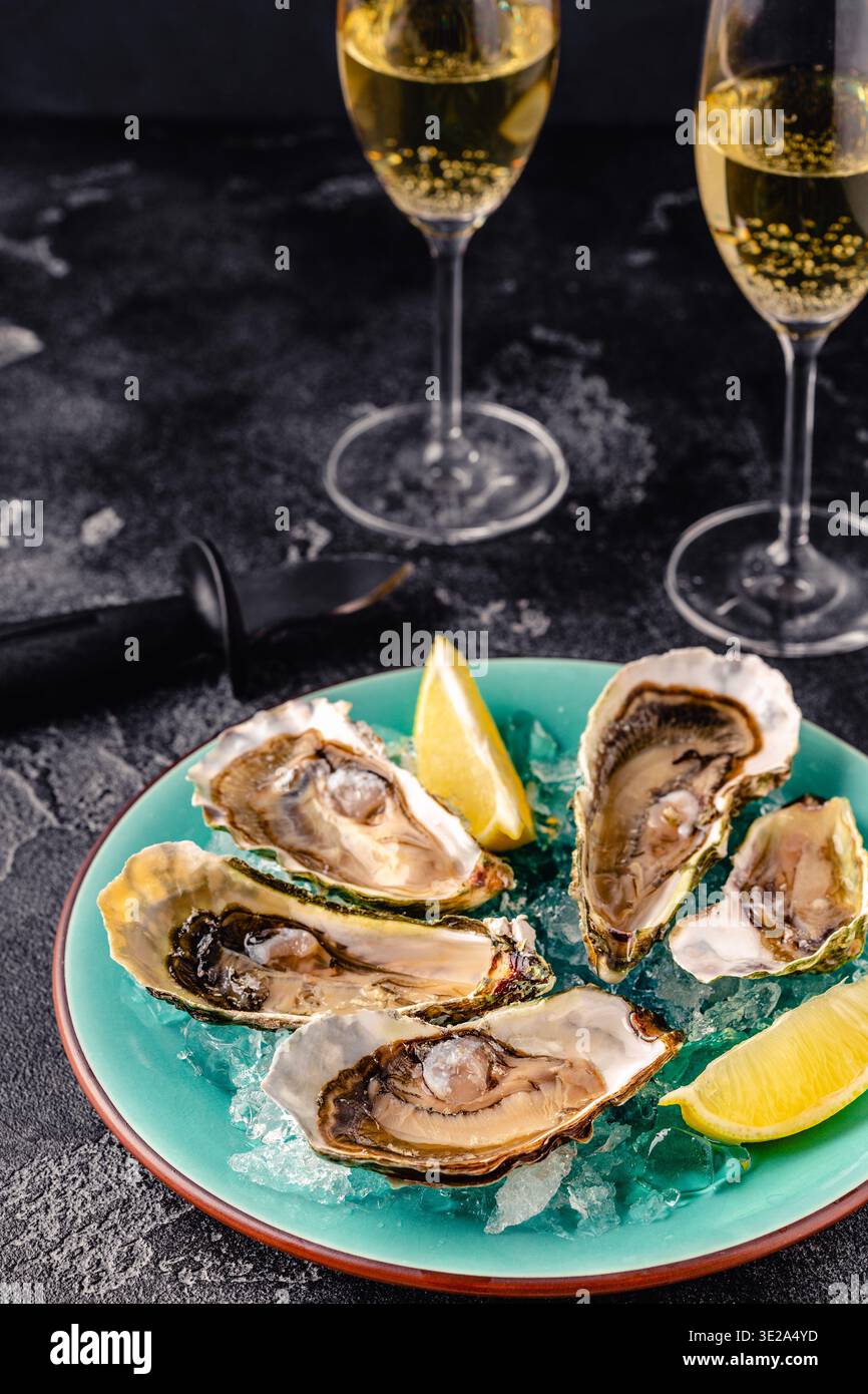 Opened fresh oysters on a blue plate, served with lemon and ice. Stock Photo