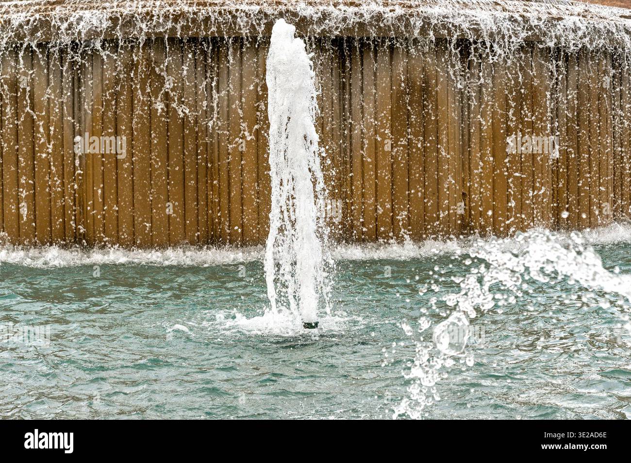 Fountain water jet shooting into a pool with cascading water over a textured wall Stock Photo