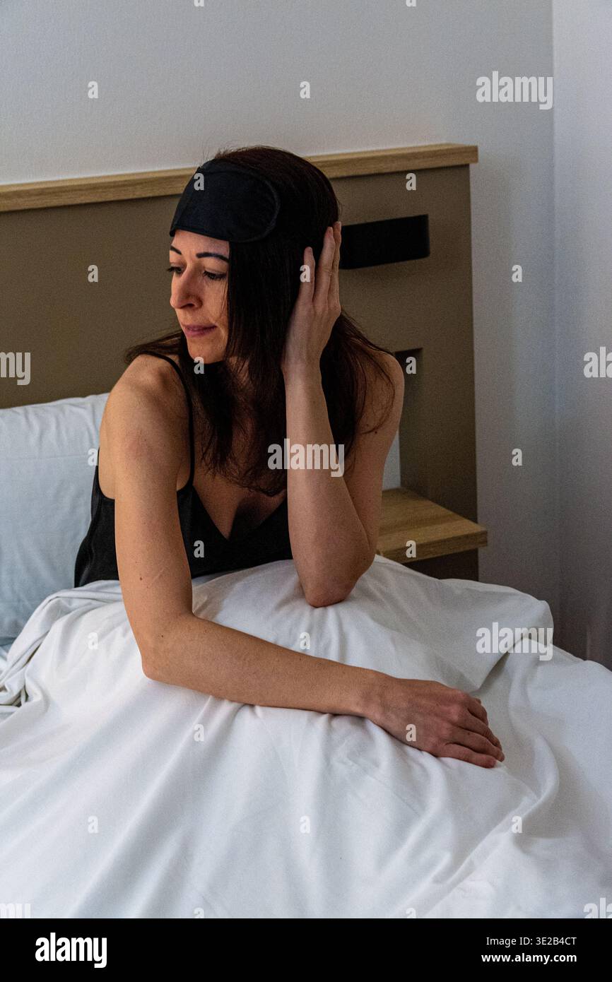 Woman waking up in bed wearing sleep mask Stock Photo
