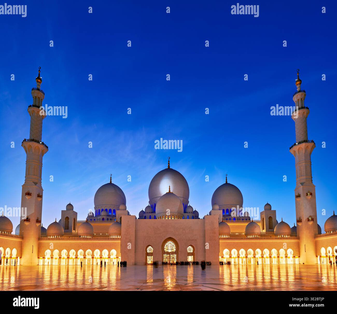 Visitors admire the grand architecture of Sheikh Zayed Grand Mosque in Abu Dhabi as night falls, highlighting its features and design. Stock Photo