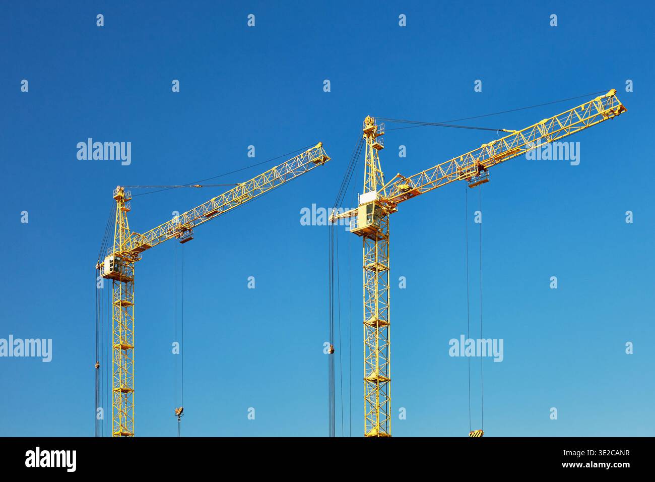 Two tall construction tower cranes against a blue sky. Stock Photo