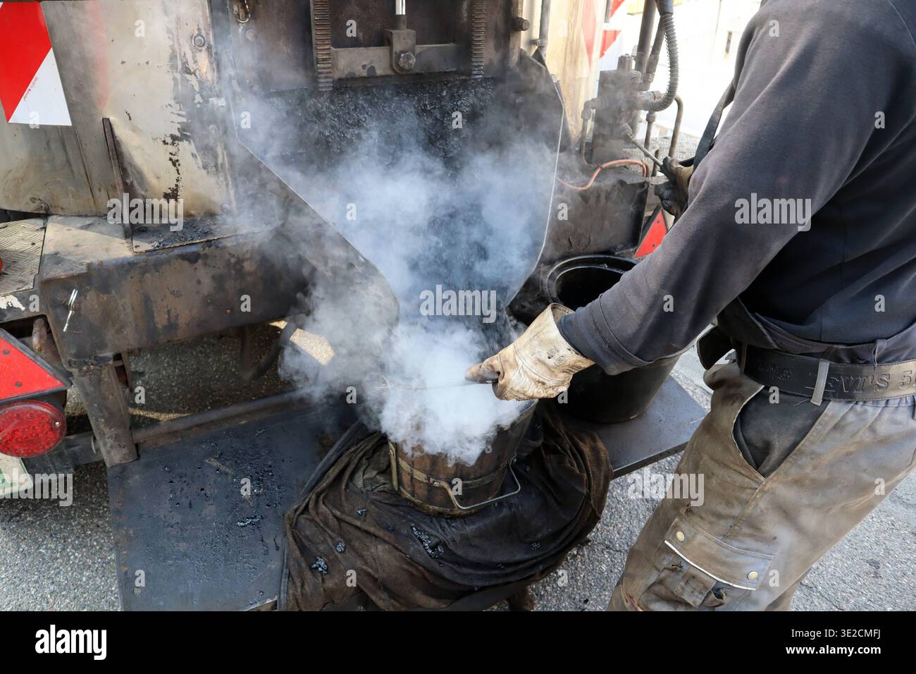 Asphaltkocher im Arbeitseinsatz Heißer Gussasphalt wird in einem Eimer vom Kocher zur Arbeitsfläche gebracht. *** Asphalt stove at work Hot mastic asphalt is brought from the stove to the work area in a bucket Stock Photo
