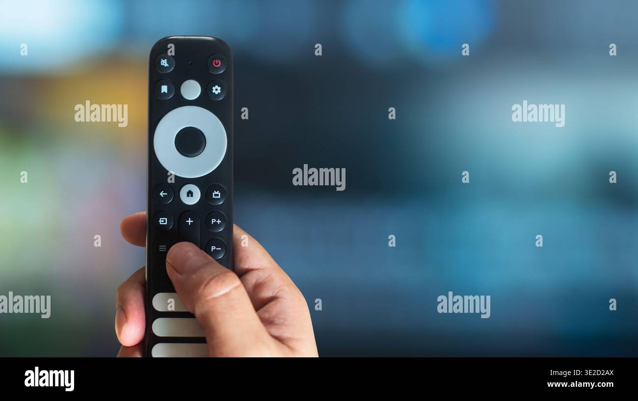 Hand Using Remote Control Hand using a modern TV remote control with copy space on a TV ...