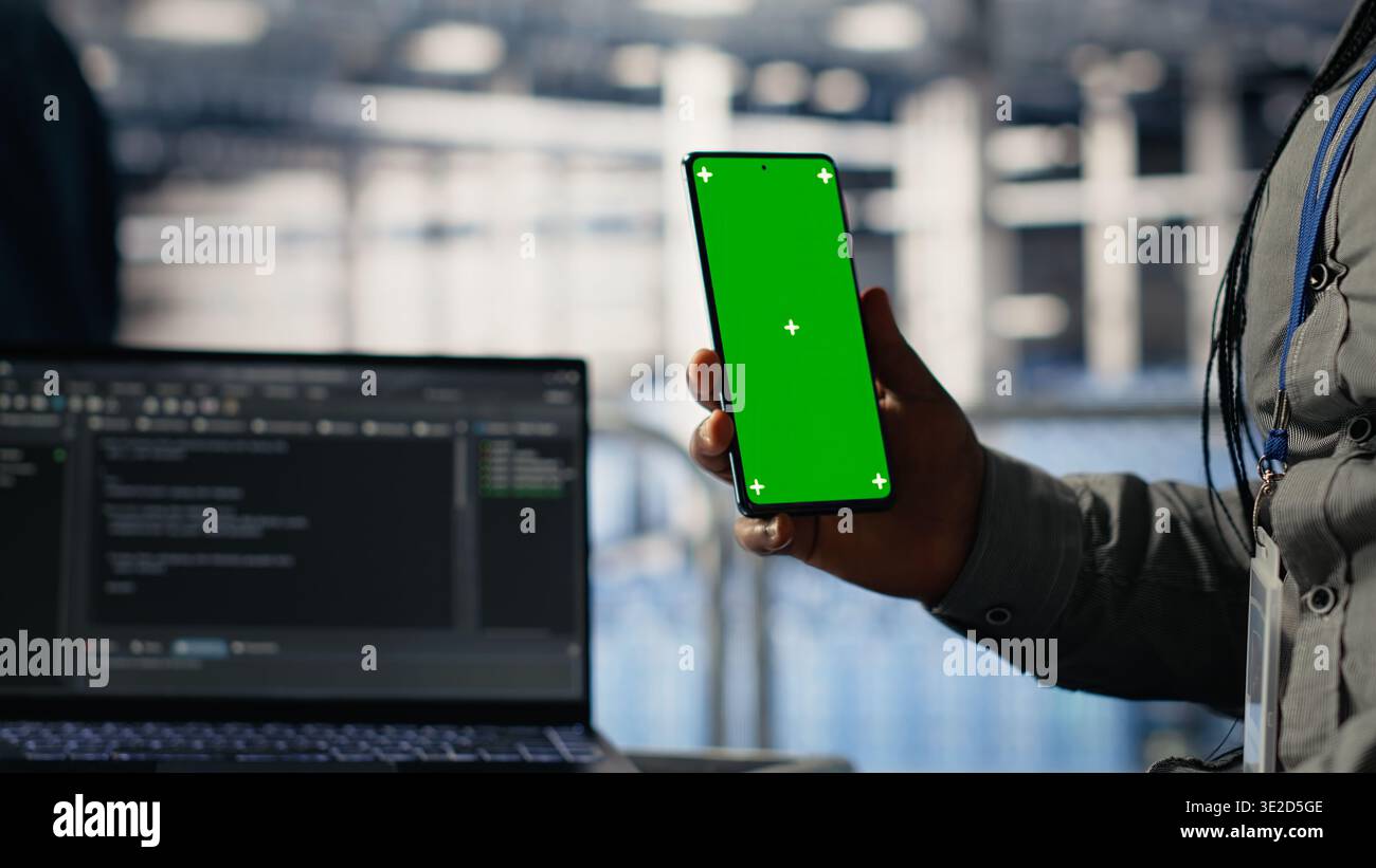 Engineer using isolated screen smartphone in server room while optimizing deep learning systems handling tasks. Data center worker uses chroma key mobile phone, adjusting AI model parameters, camera B Stock Photo