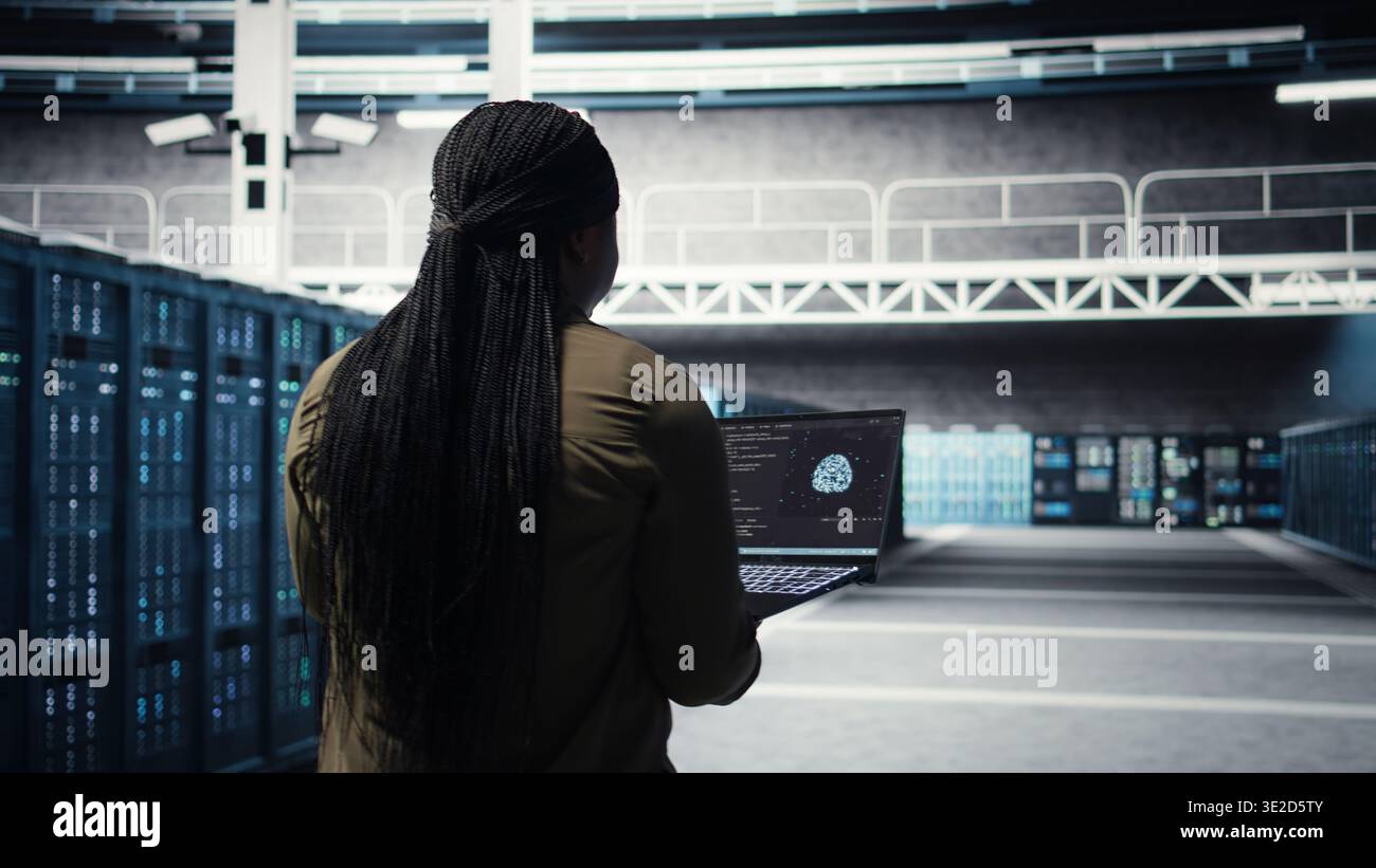 Engineer in server hub using laptop to upgrade rigs for increase in workload capacity using AI deep learning. Data center employee uses artificial intelligence to improve processing speed, camera A Stock Photo