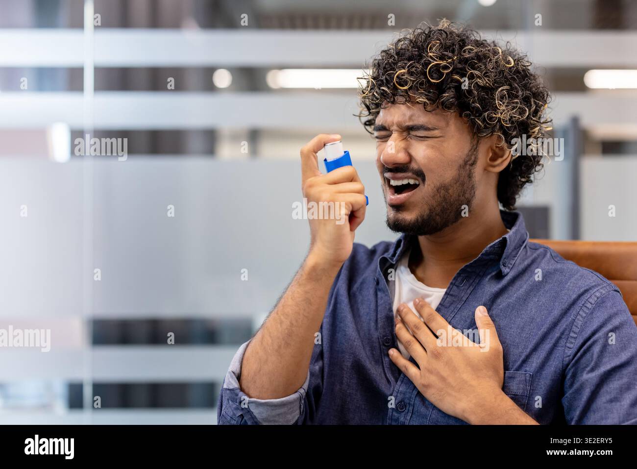 Indian young man using inhaler at workplace. Stock Photo