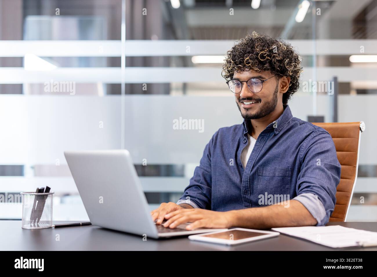 Smiling Indian man working in the office at a laptop. Stock Photo