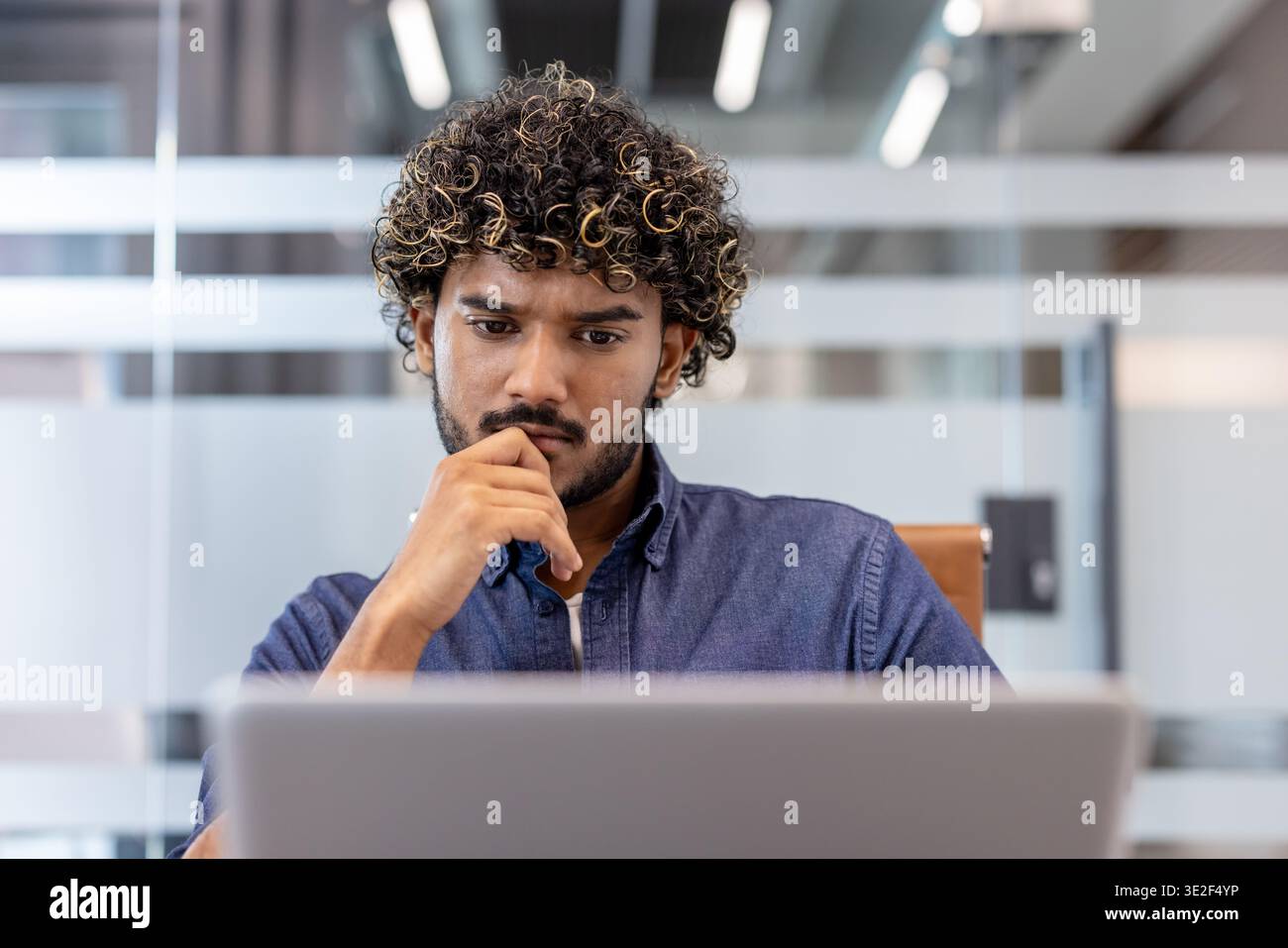 Thoughtful and focused young Indian man working in the office on a laptop. Stock Photo