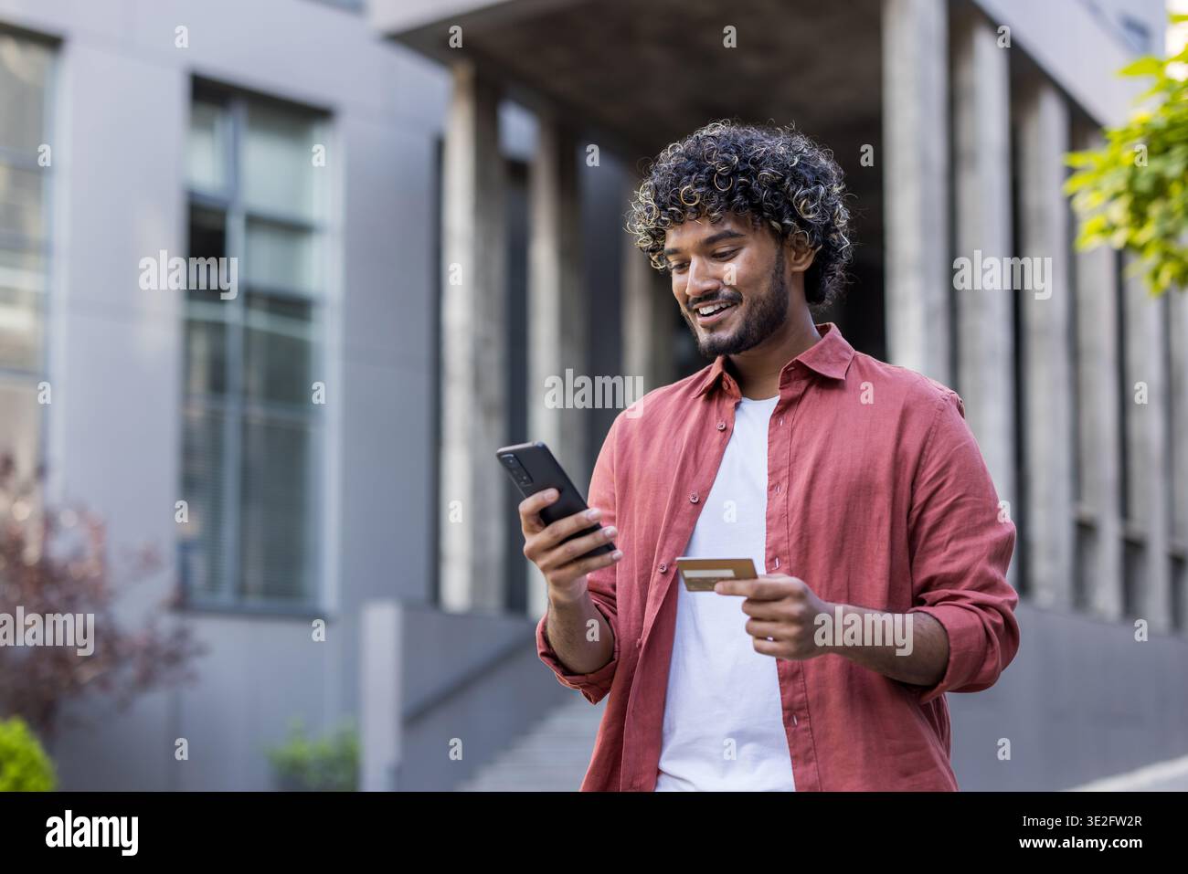 Young Indian man standing on the street, using mobile phone and credit card. Stock Photo