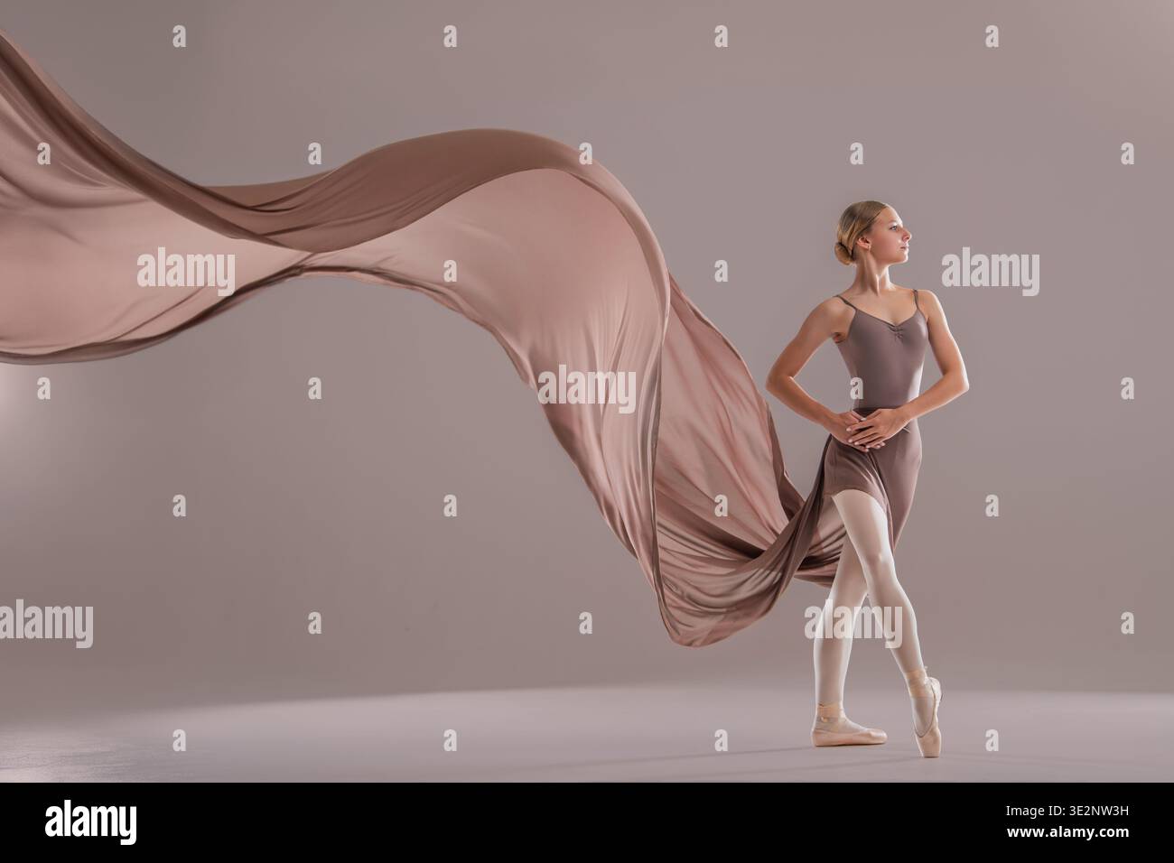 Young ballerina posing with flowing beige fabric in studio Stock Photo