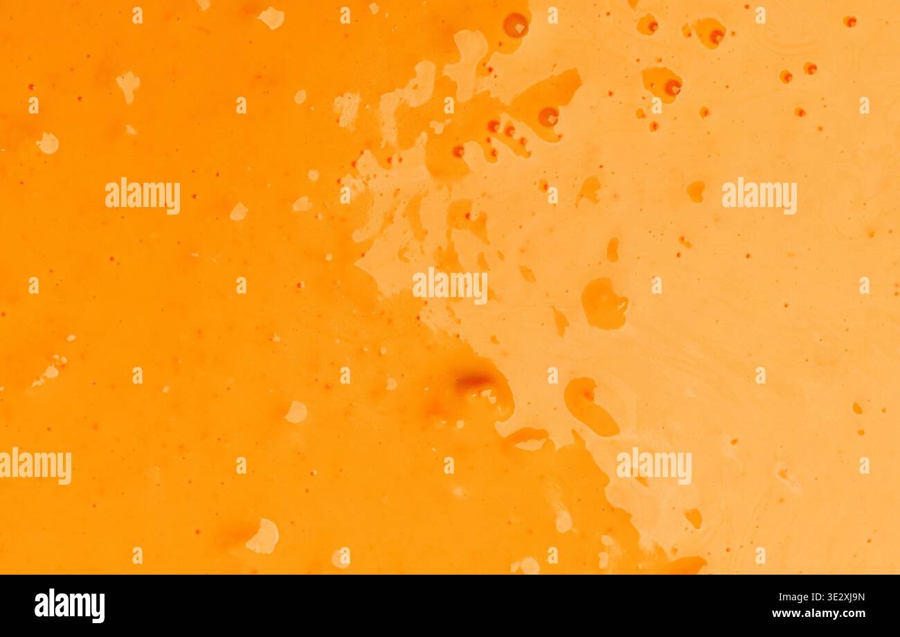 Orange liquid paint splashing on a surface creating a vibrant texture Stock Photo