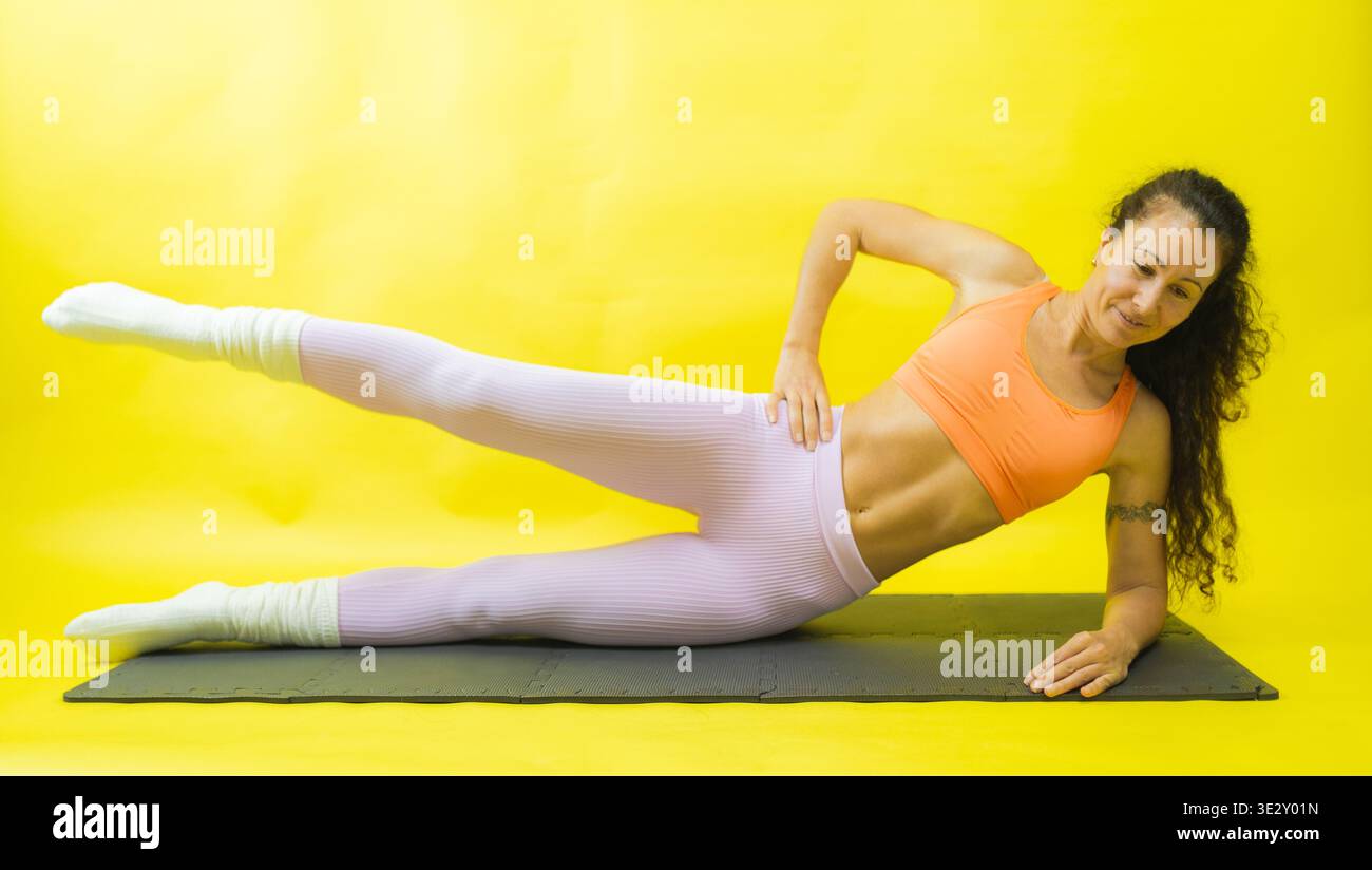 Woman performing side leg raise exercise on exercise mat Stock Photo