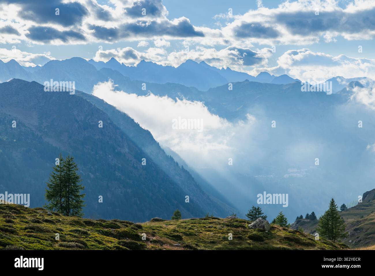 Majestic mountain range with clouds and sun rays illuminating the valley in the Italian Alps Stock Photo