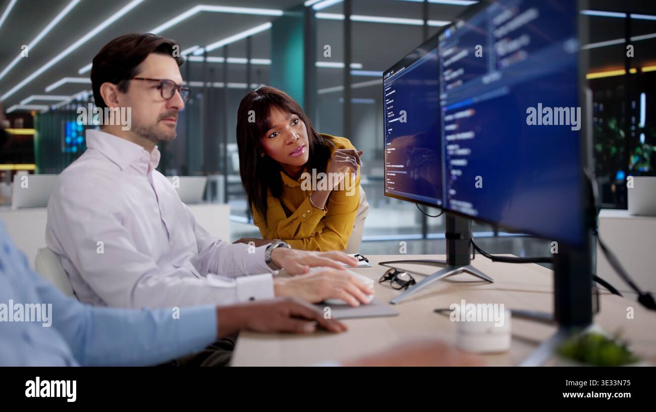 Diverse Tech Team Collaborates Closely Coding Software At Busy Office Desks. Several People, Including A Programmer Stock Photo