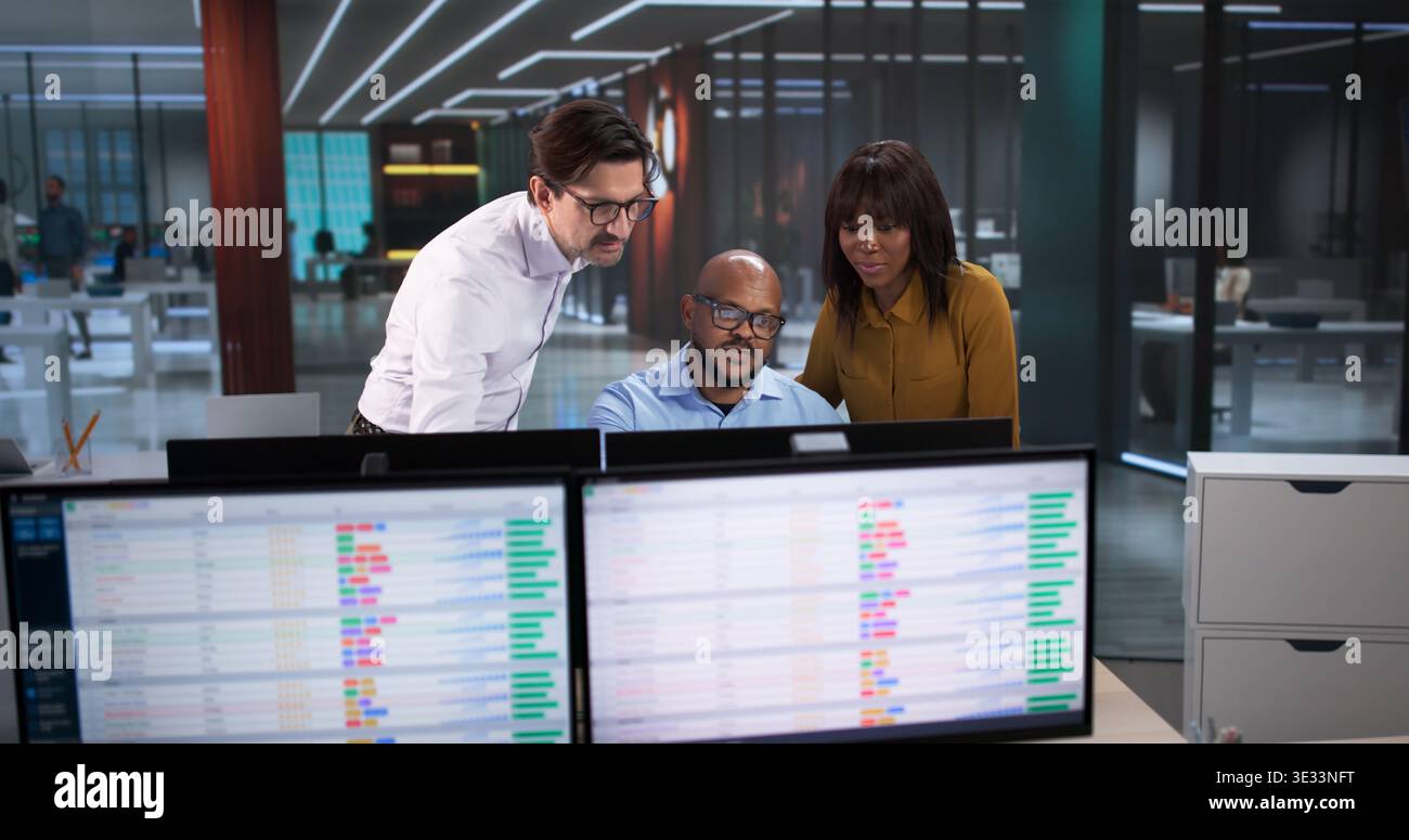 Young Analyst And Team Using Computers, Reviewing Data Spreadsheets, And Coding Reports In A Modern Office Stock Photo