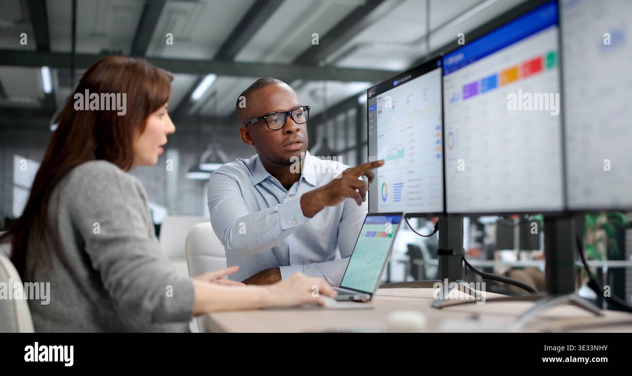 Two Young Professionals Collaborate On ERP And CRM Software, Discussing Data Analysis Stock Photo
