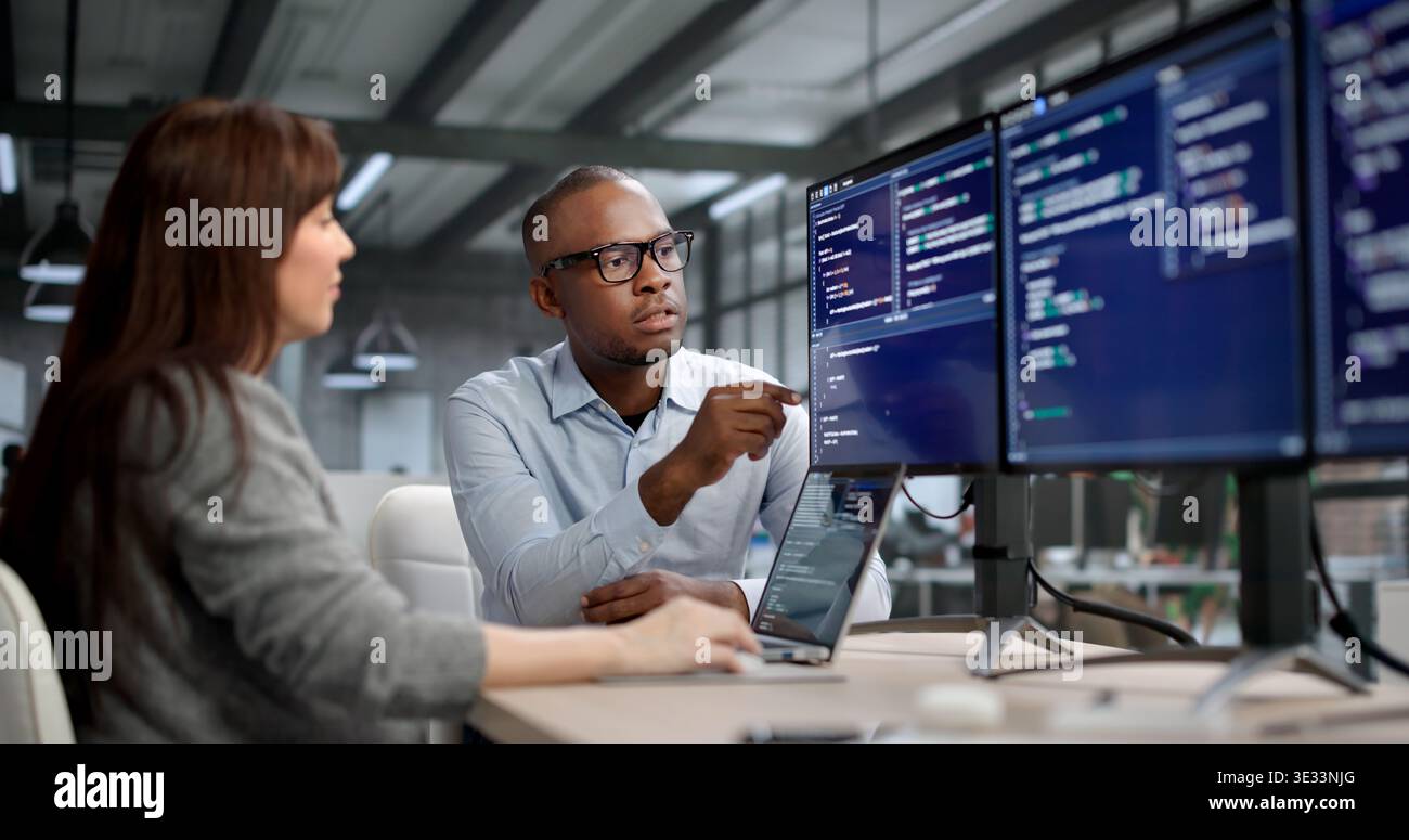 Female Software Developer Codes On Computer While A Manager Leads Training Stock Photo