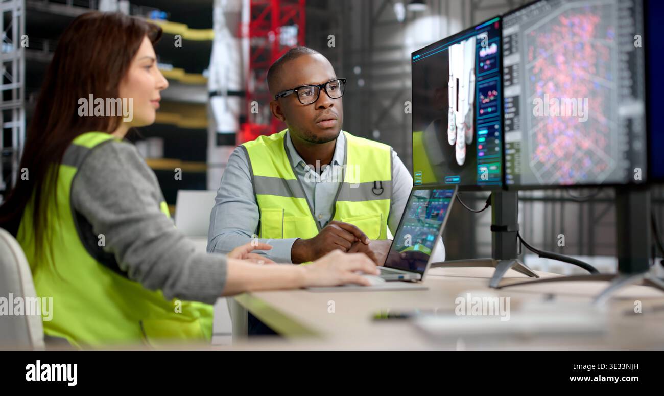 Two Engineers, A Man And Woman, Discuss Rocket Engine Designs On A Big Computer Screen Using 3D CAD Software Stock Photo