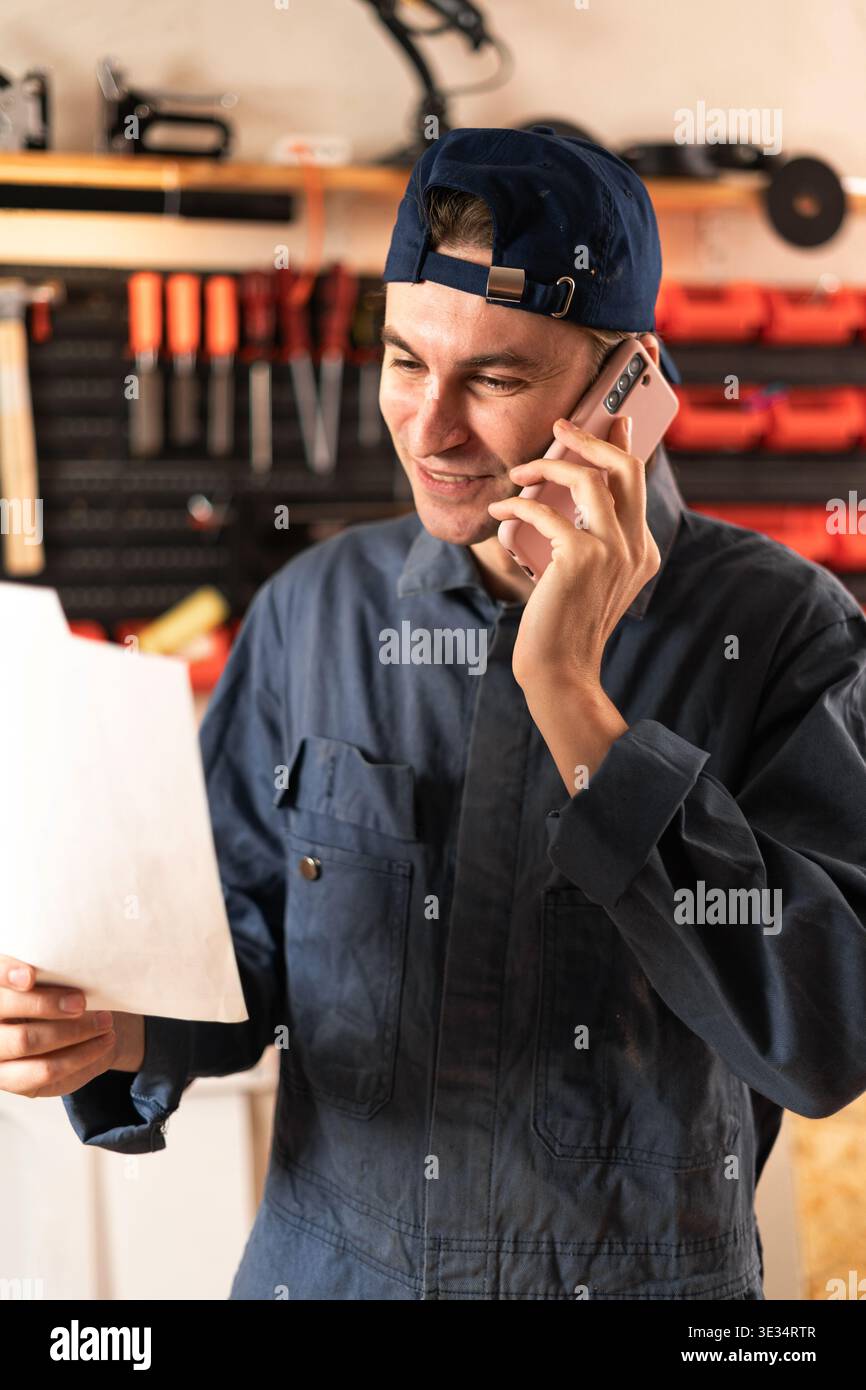 Repairman or mechanic examining paperwork and communicating using mobile phone working in garage. copy space Stock Photo