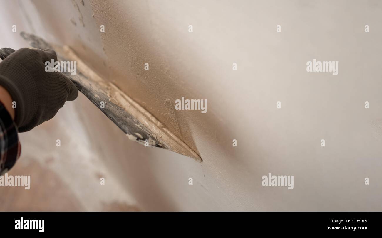 Professional builder applying white putty layer on wall surface during renovation. close-up Stock Photo