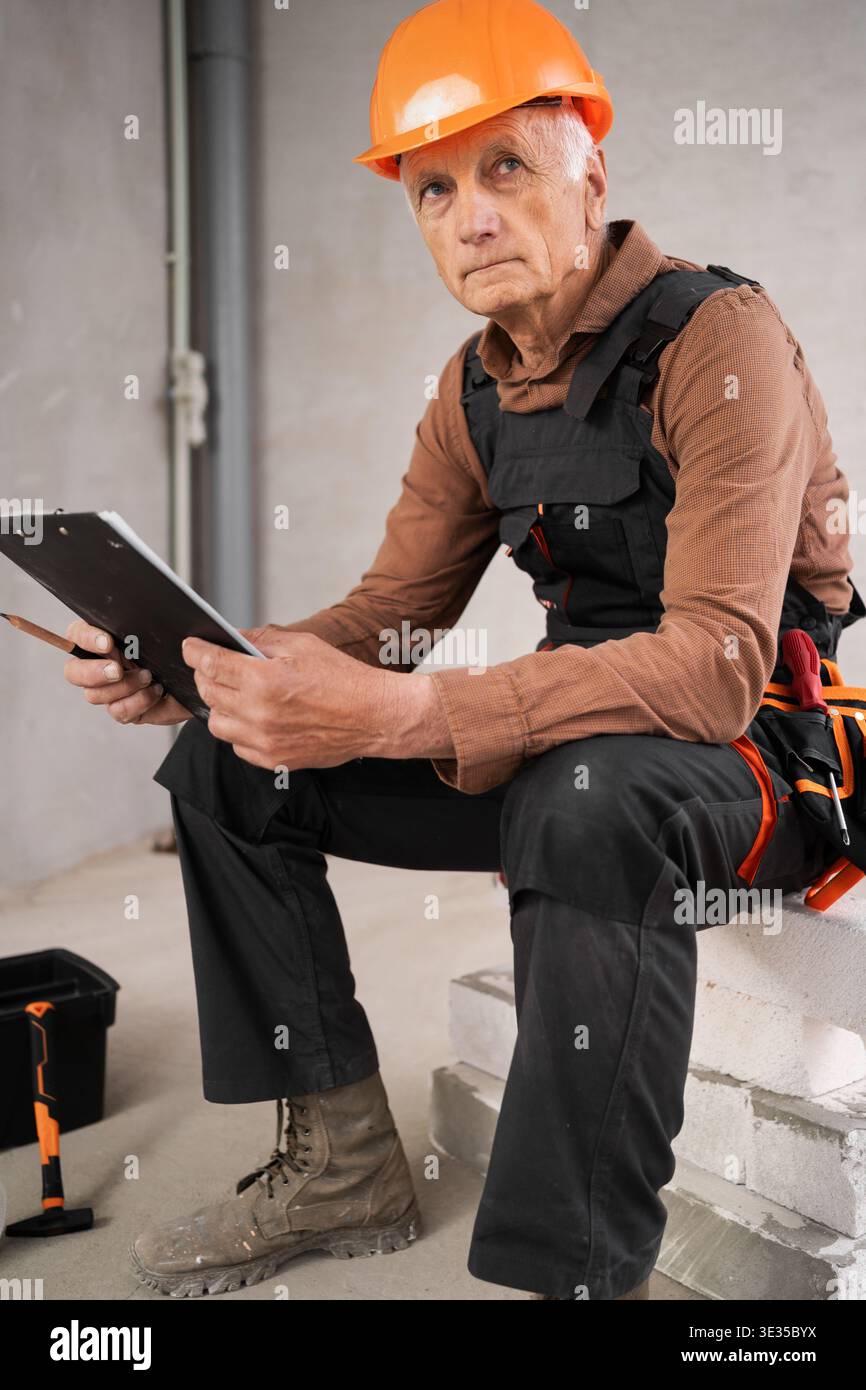 Portrait of pensive builder or repairman senior man in safety helmet on building site during renovation process. profession, construction and repair c Stock Photo