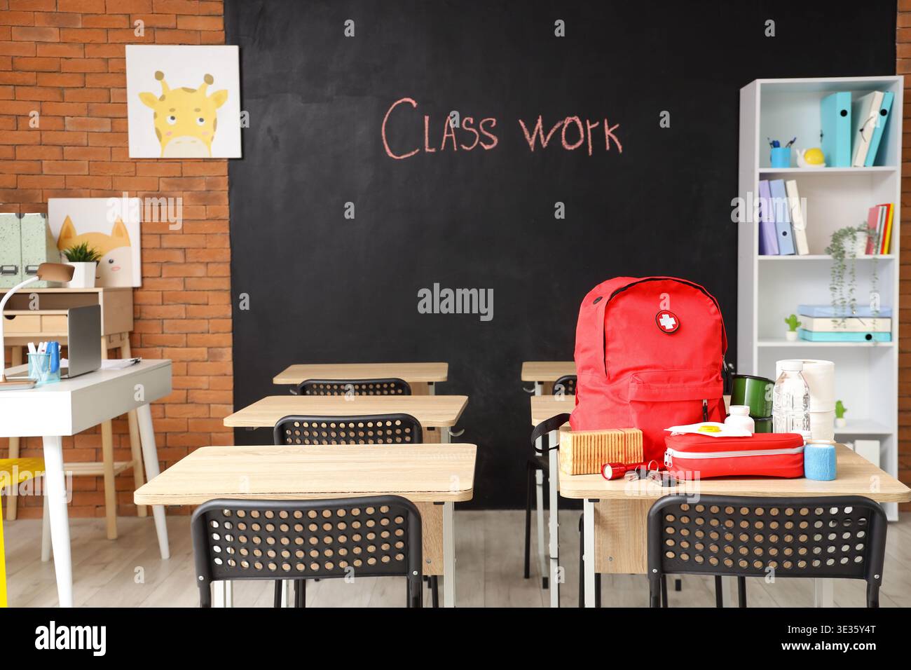 Emergency backpack, first aid kit and necessities on table in empty classroom Stock Photo