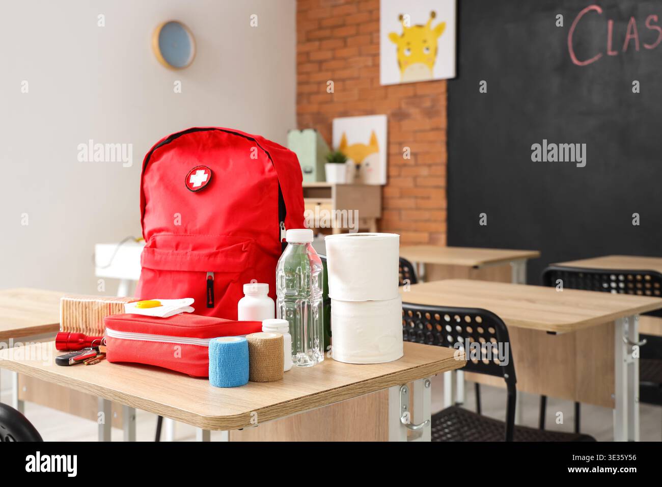 Emergency backpack, first aid kit and necessities on table in empty classroom Stock Photo