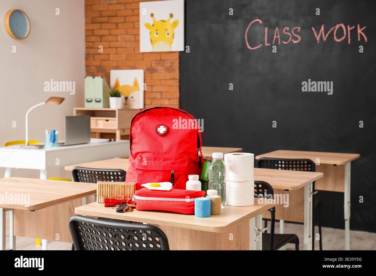 Emergency backpack, first aid kit and necessities on table in empty classroom Stock Photo