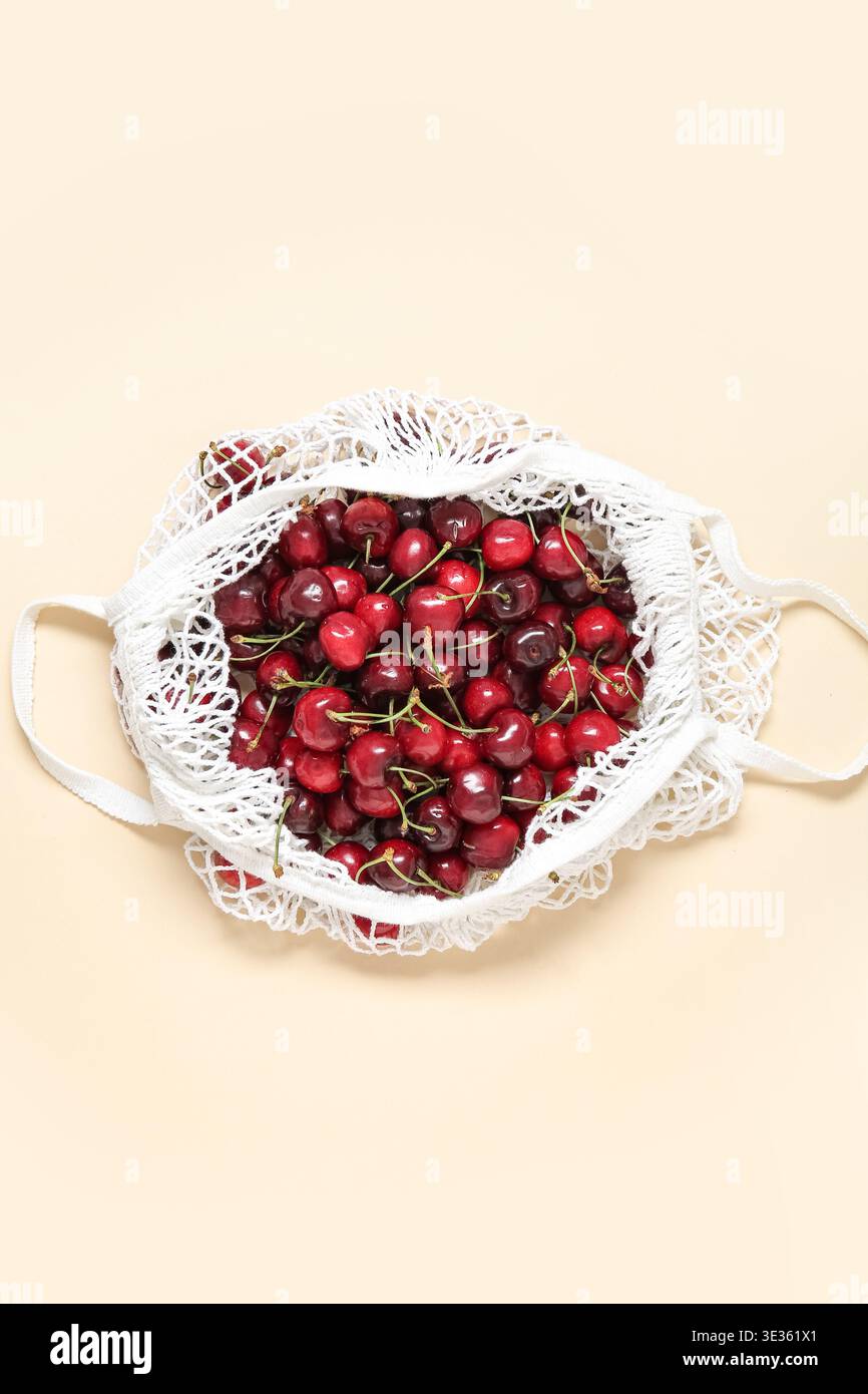 Mesh bag with fresh cherry on beige background Stock Photo