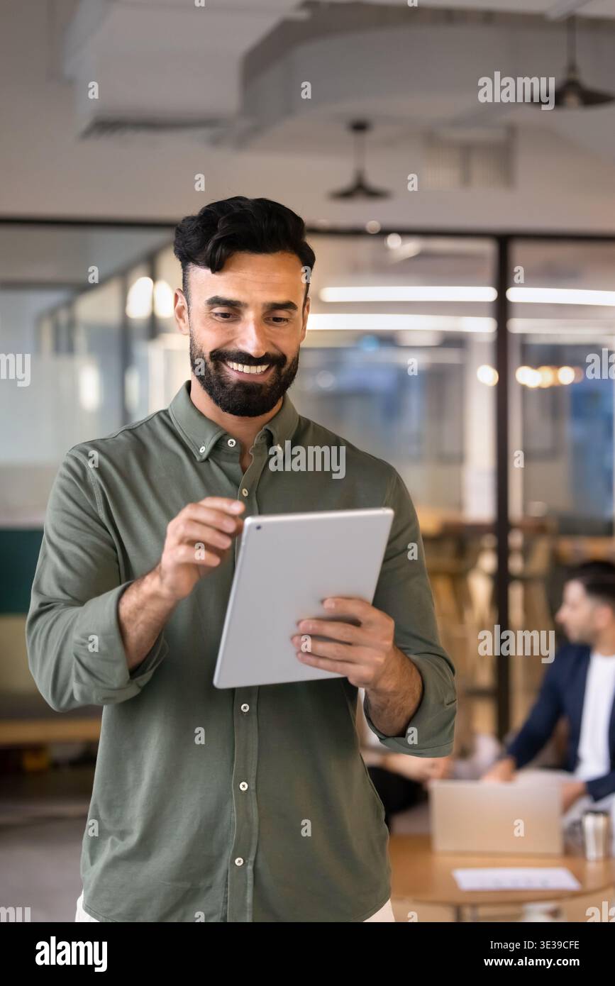 Smiling Middle Eastern businessman using digital tablet stands in office Stock Photo