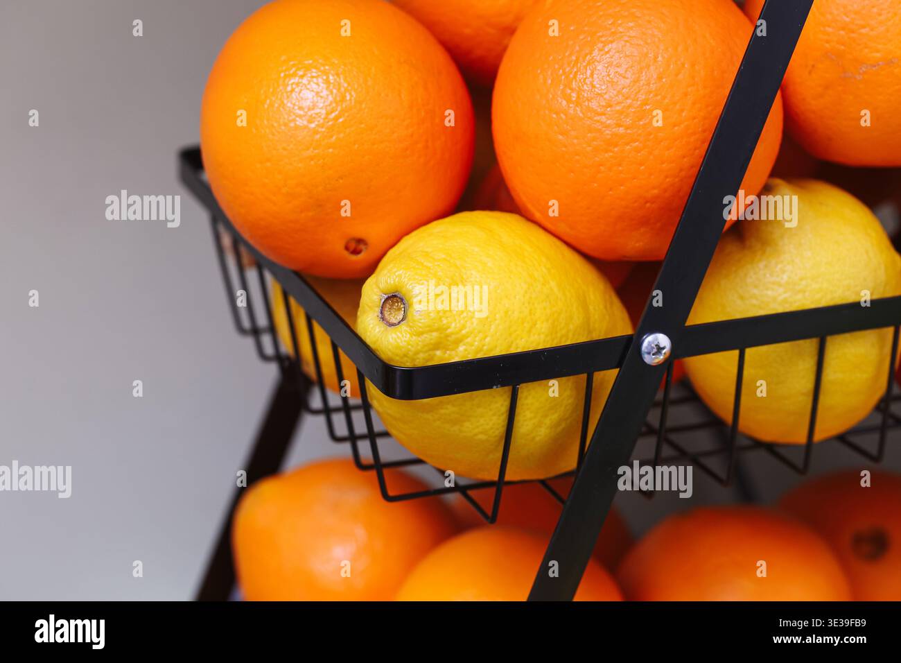 Fresh oranges and lemons in a black wire basket. Healthy citrus fruits in a simple kitchen setting. Natural vitamins and fresh food concept Stock Photo