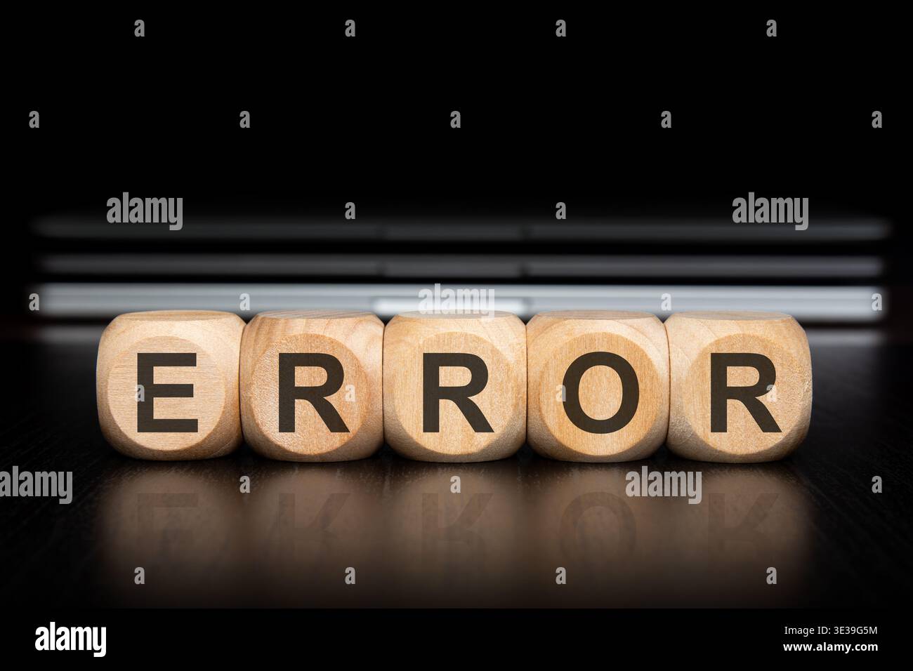 Close up of wooden toy blocks spelling the word ERROR with a clear reflection on a dark polished desk. In the blurred background, a stack of modern gr Stock Photo
