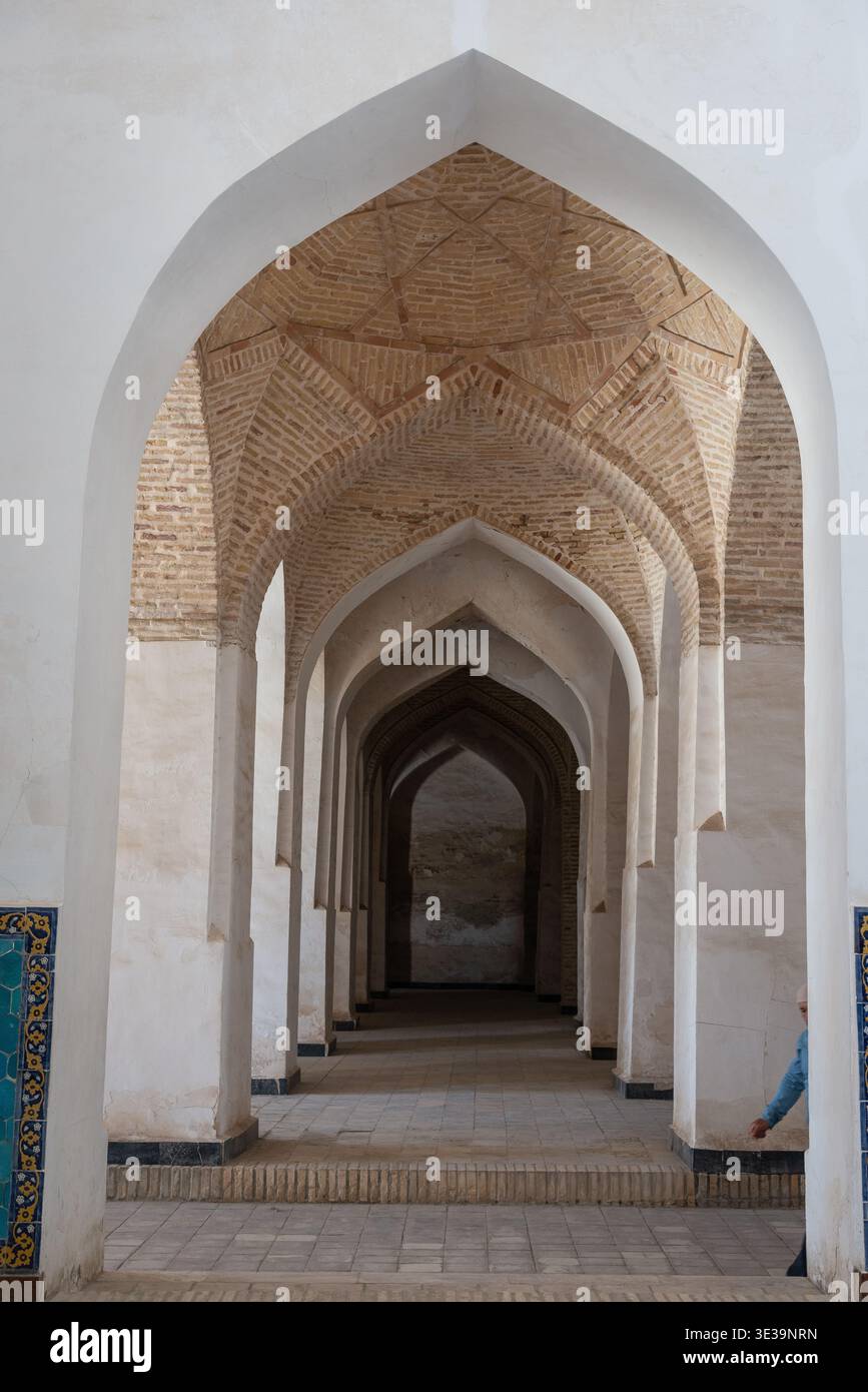 Brick corridor with repeating pointed arches and intricate tilework, creating a deep geometric perspective under warm light Stock Photo