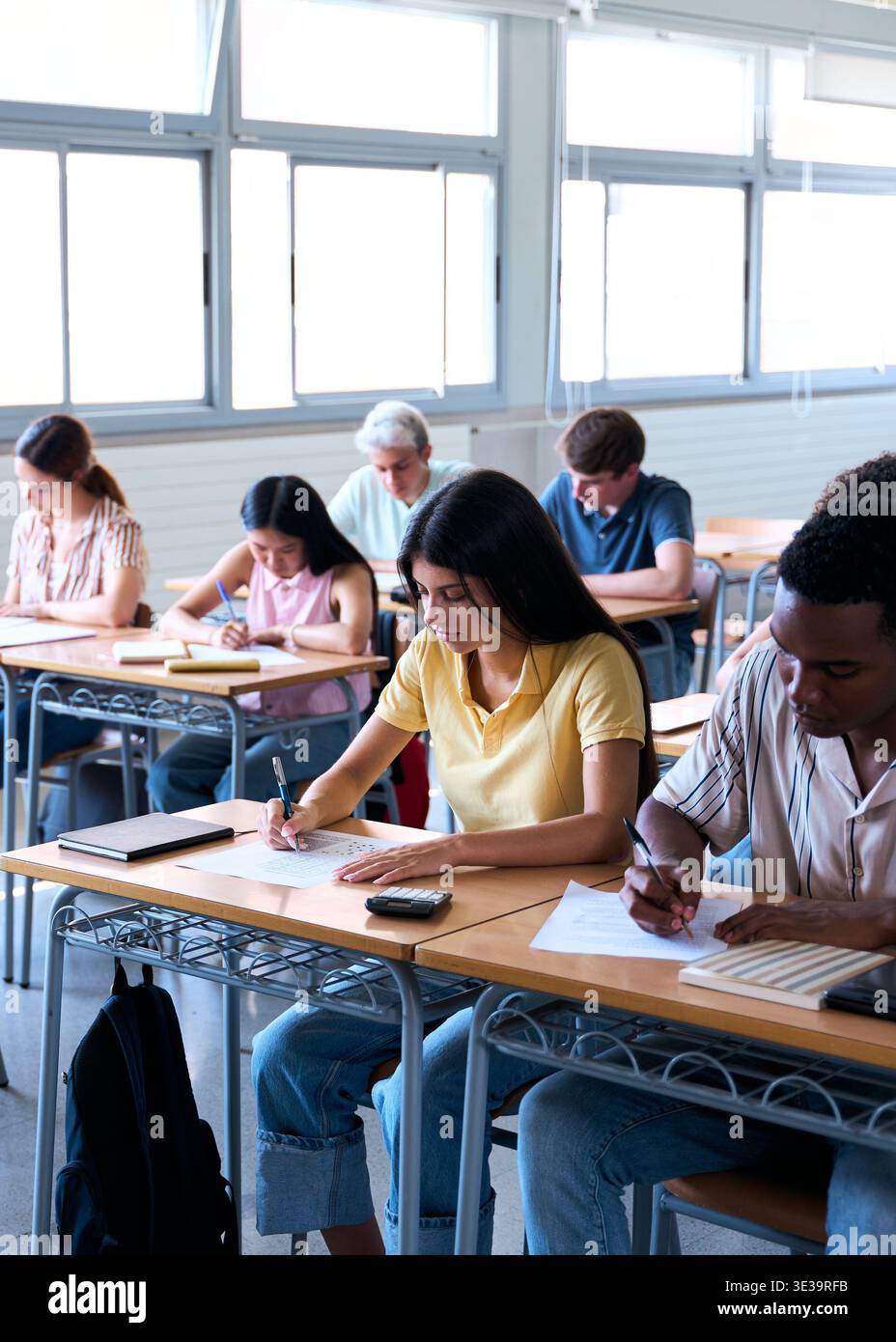 Students taking exam while teacher supervises in classroom Stock Photo