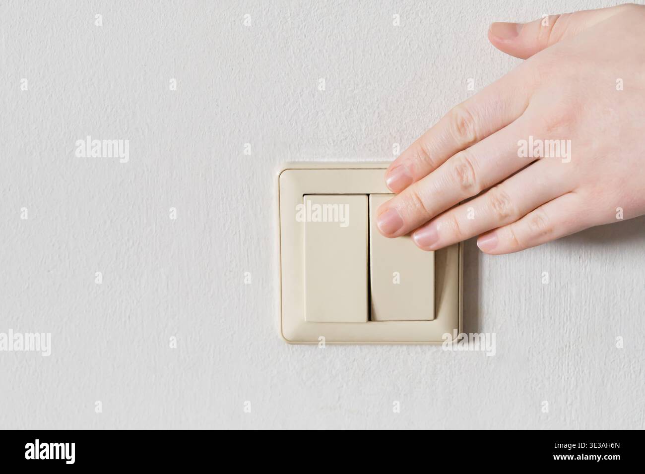 Hand turning off light switch on white wall, saving electricity Stock Photo