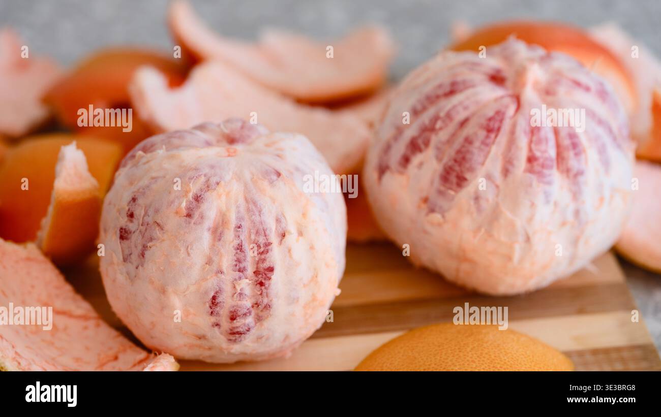 Two peeled whole grapefruits on a wooden cutting board surrounded by pieces of citrus peel. Close-up Stock Photo