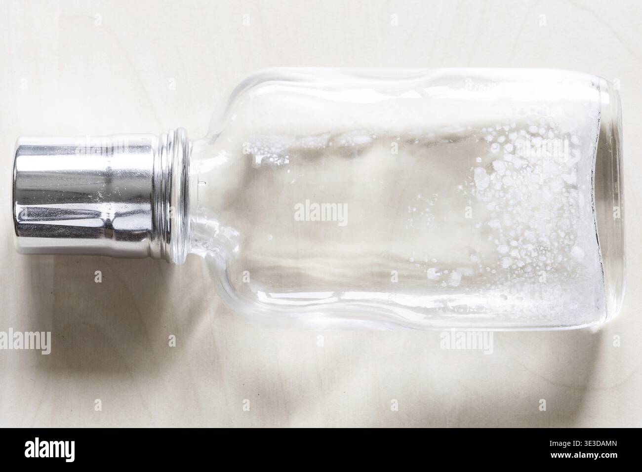 Lying empty glass bottle with white spots from the glass disease on a wooden table Stock Photo