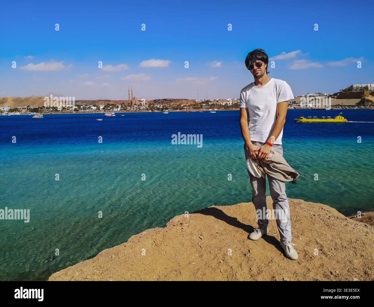 Young dark-haired European man poses over a cliff against the backdrop of the Red Sea in Sharm El Sheikh (Egypt). Handsome adult guy stands on a rock - Smartphone Captured Stock Image