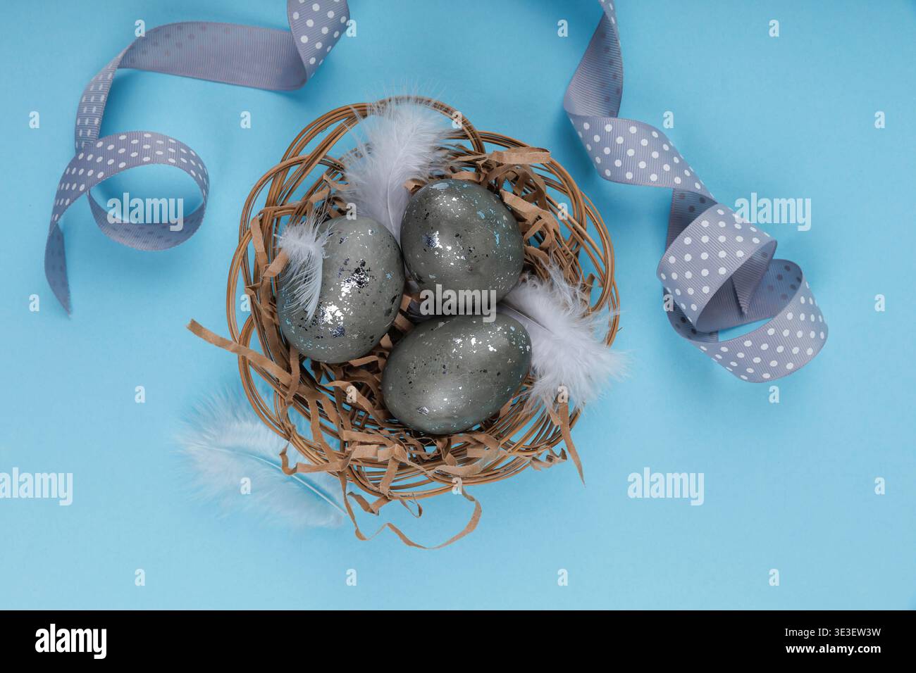 Easter eggs nest composition with ribbon on blue background Stock Photo