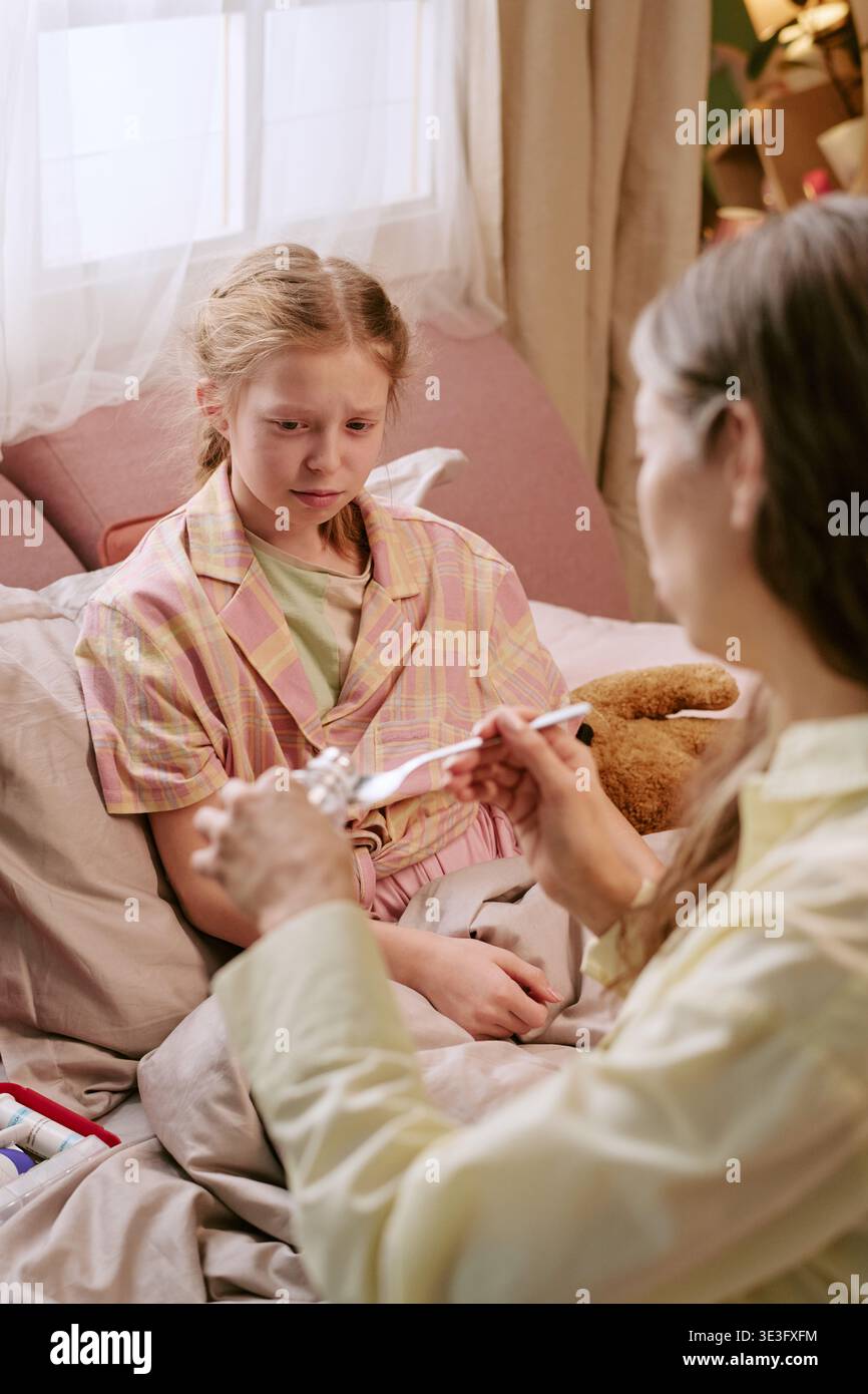 Girl Sitting in Bed Watching Middle Aged Woman Preparing Medicine Stock Photo