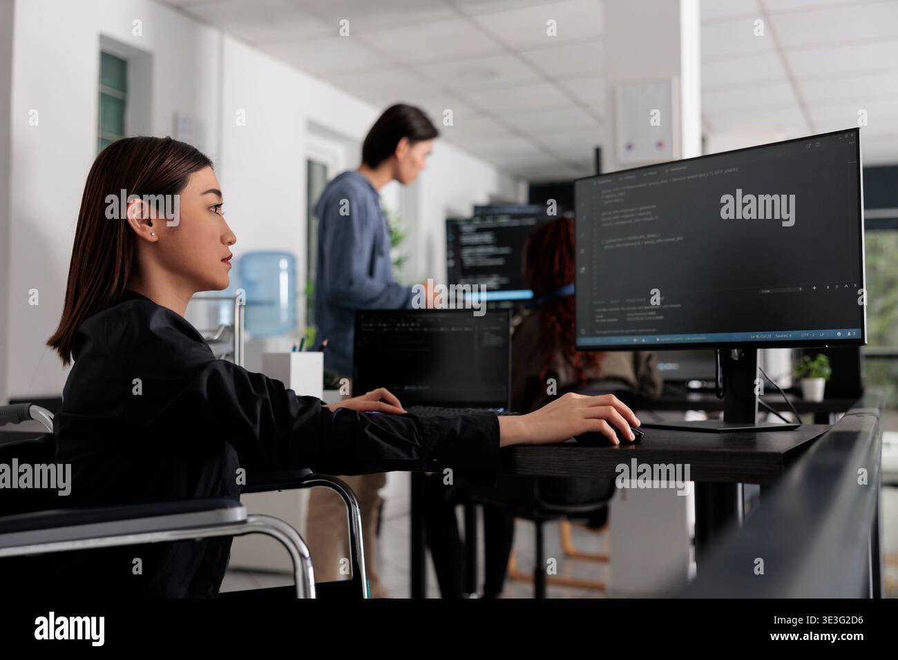 Web developer in wheelchair working on server coding in big data office, analyzing programming language and script on terminal window. Disabled woman programmer with impairment working on it system. Stock Photo