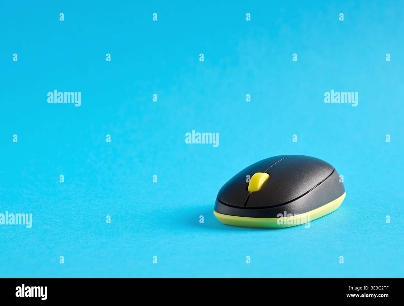 Modern wireless computer mouse with yellow scroll wheel on a bright blue background, representing technology and connectivity Stock Photo