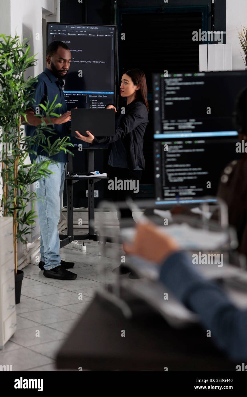 Diverse team of software programmers analyzing html code on wall screen tv, using digital gadget and working with artficial intelligence. Coders parsing cloud computing project with big data. Stock Photo