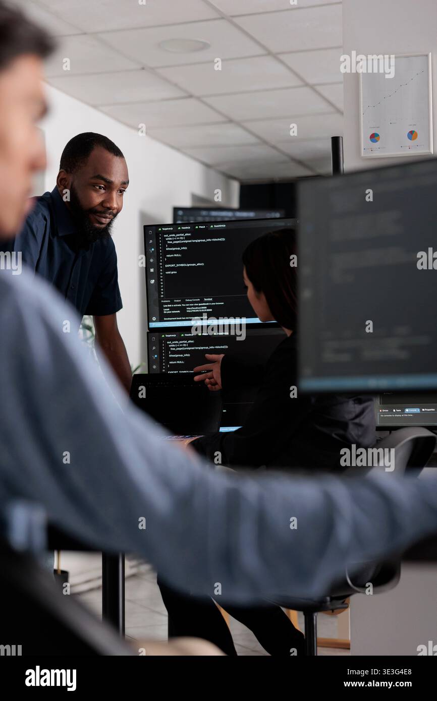Multi ethnic team of software developers talking about html code in it company office. Artificial intelligence cloud programers compiling algorithms on terminal window server, doing teamwork Stock Photo