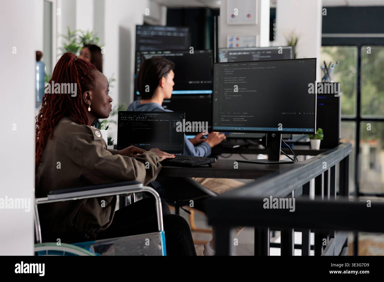 Wheelchair user typing script code on computer, working with cloud computing terminal window. Disabled web developer writing artificial intelligence algorithm in it big data company office. Stock Photo