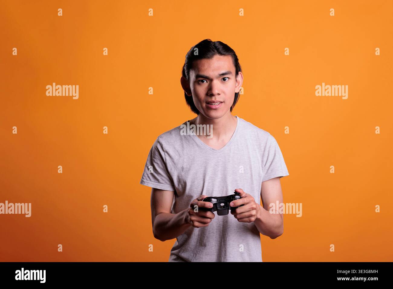 Teenager playing video games with joystick, entertainment activity. Concentrated young asian man holding gamer gadget, person using console wireless controller, enjoying videogames Stock Photo