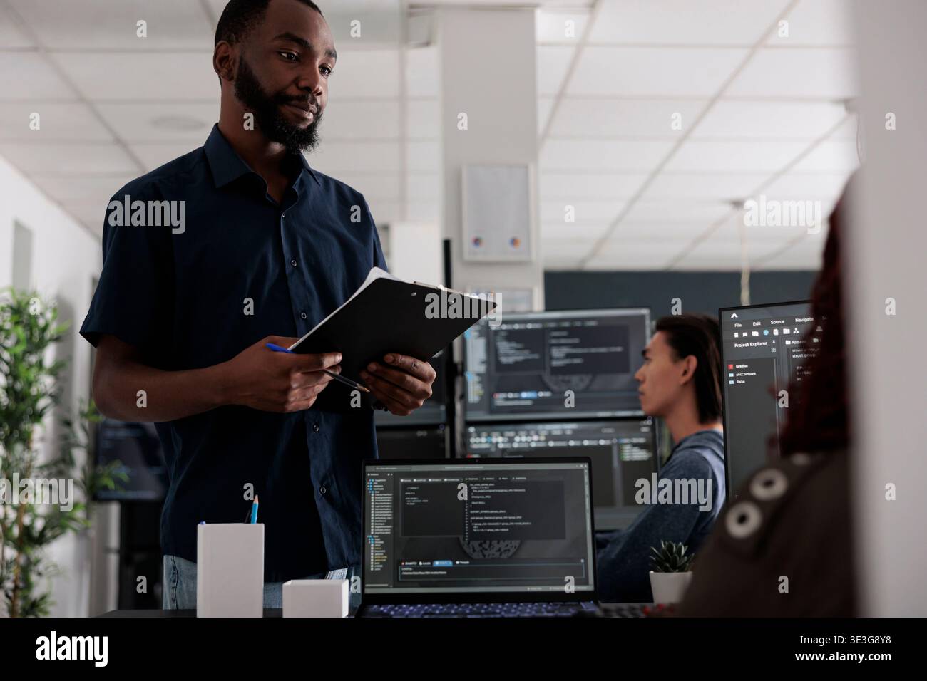 Software developer holding clipboard checking html code on terminal window, using server database on computer. Coders talking about programming language and cloud computing user interface. Stock Photo