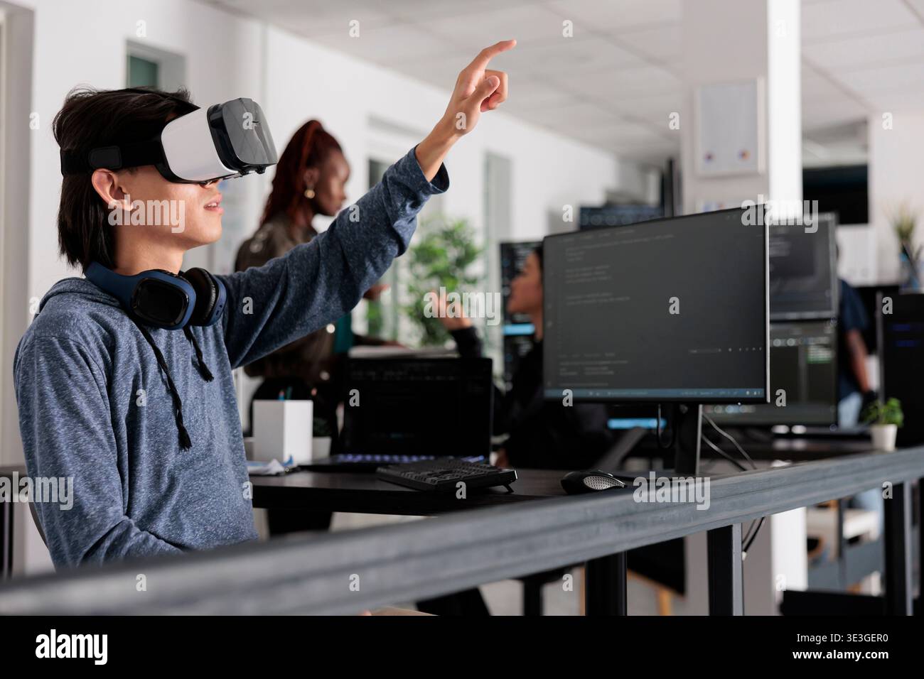 Asian software developer using virtual reality goggles to code new server interface, analyzing script information on terminal window. Coder programming it database for internet software with vr headset. Stock Photo
