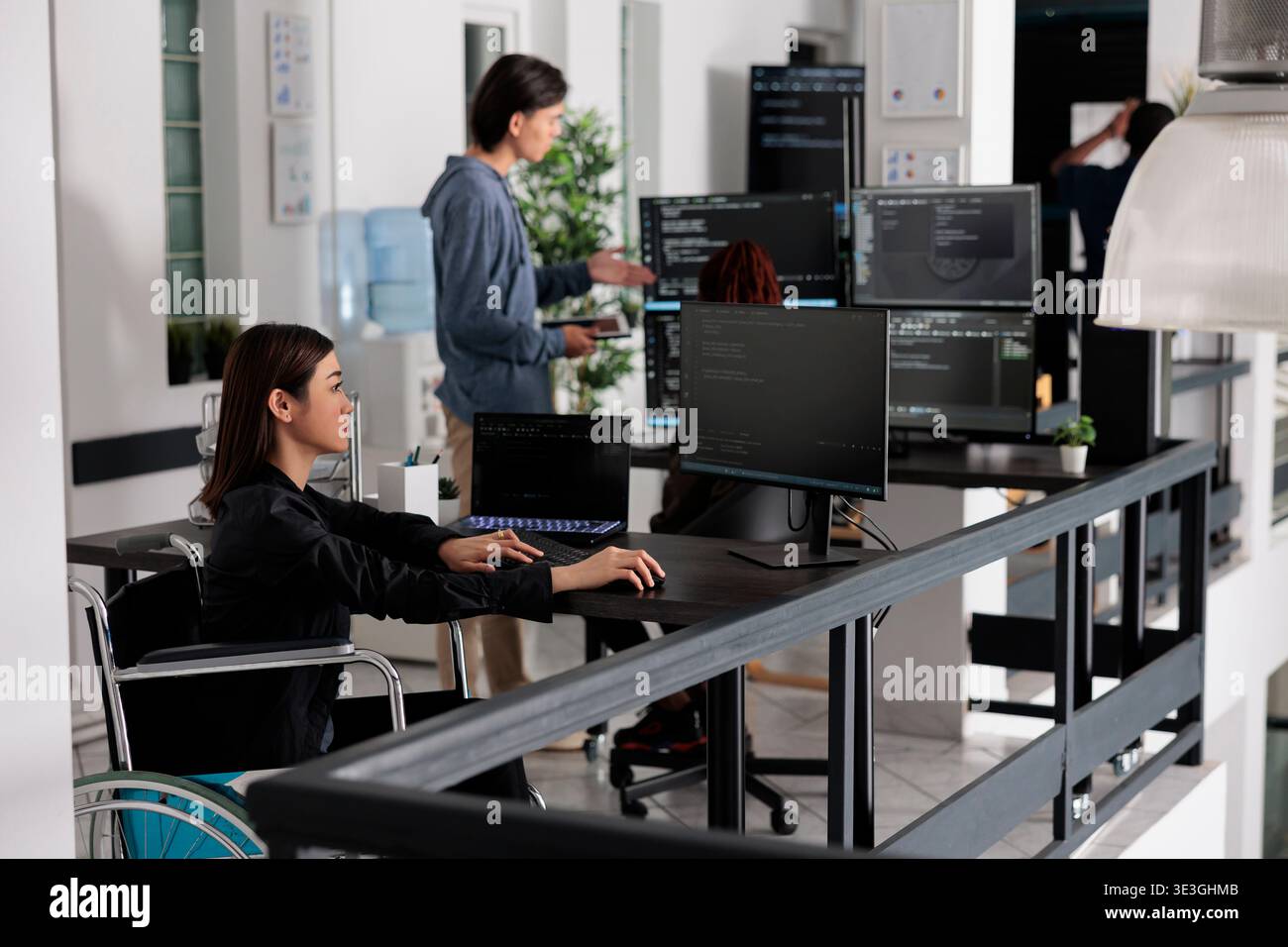 Focused software developer in wheelchair writing server code in coding agency room, using security system. Asian engineer with physical disability programming user interface ai office. Stock Photo
